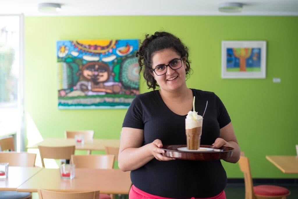 Eine Frau lächelt freundlich in die kamera und hält dabei ein Getränk in der Hand.